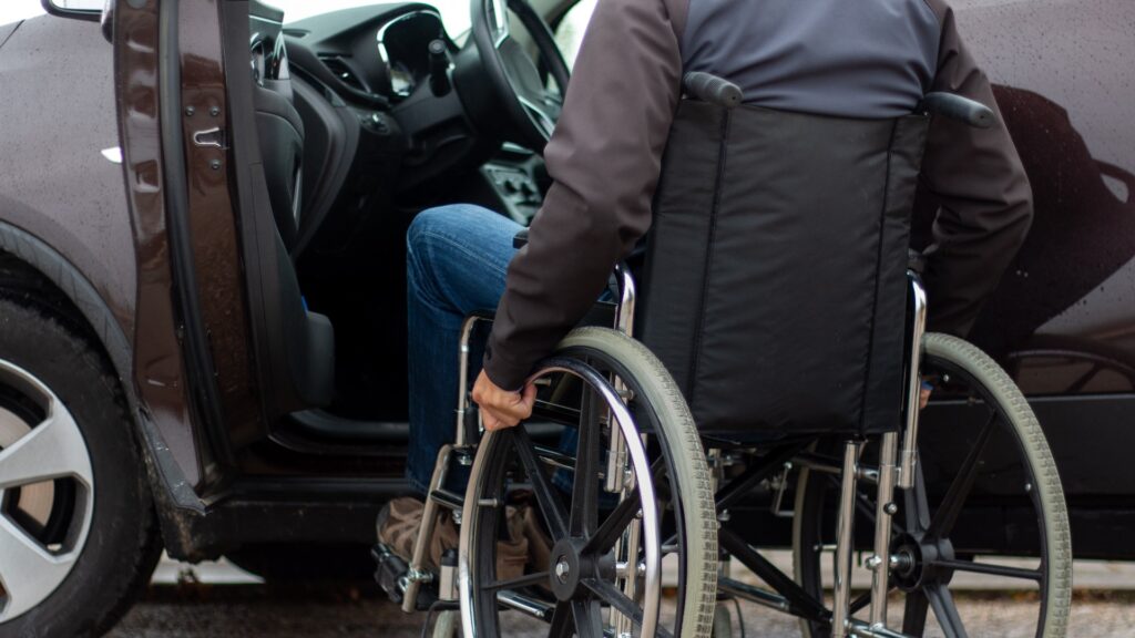 Ein Mann im Rollstuhl versucht, sich auf den Fahrersitz eines Autos zu setzen.