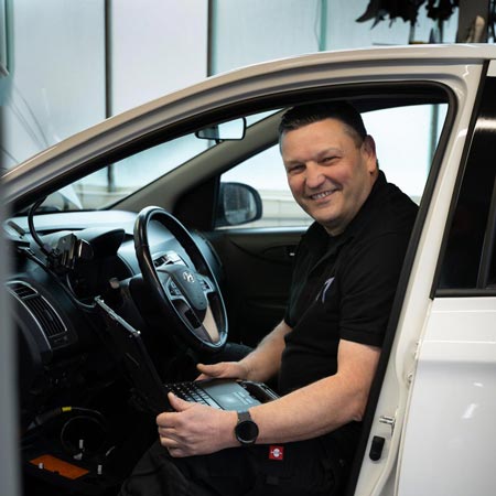 Mann mit neutralem Blick in weißem Auto, nutzt schwarzen Laptop am Lenkrad